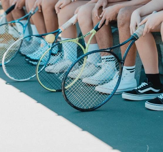 People sitting on a bench holding tennis rackets