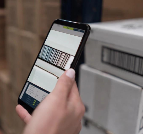 Person using mobile phone to scan barcode in warehouse, linked to NetSuite warehouse management system.