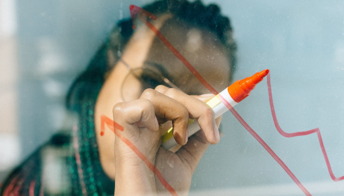 Close up of woman using red pen on transparent board to indicate an upward financial trend due to the cost effectiveness of cloud software.