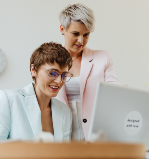 Two business women at a desk looking at the new rebates and trades promotion NetSuite feature, released as part of the 2022.2 update.