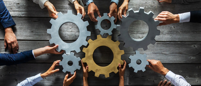 Six pairs of hands holding on to six interconnected cogs to denote integrated ERP functionality within NetSuite, Sage, SAP and Microsoft.