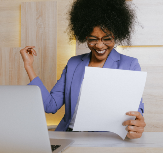 Woman sat at a desk holding a piece of paper with a huge smile because her business VAT compliance KPIs are showing success.