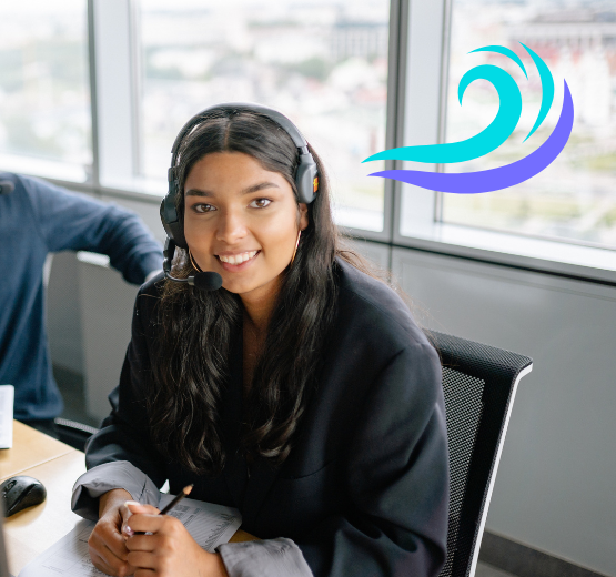 Woman sat at a desk wearing a headset, she is smiling because she is using the new features within the Microsoft Dynamics 365 Release Wave 1 of 2023.