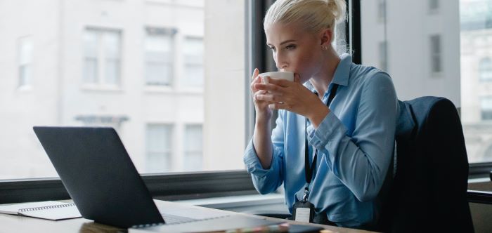 A female accounting progessional sat at her desk drinking a coffee, looking at her laptop enjoying the new features in NetSuite Release 2023.2.