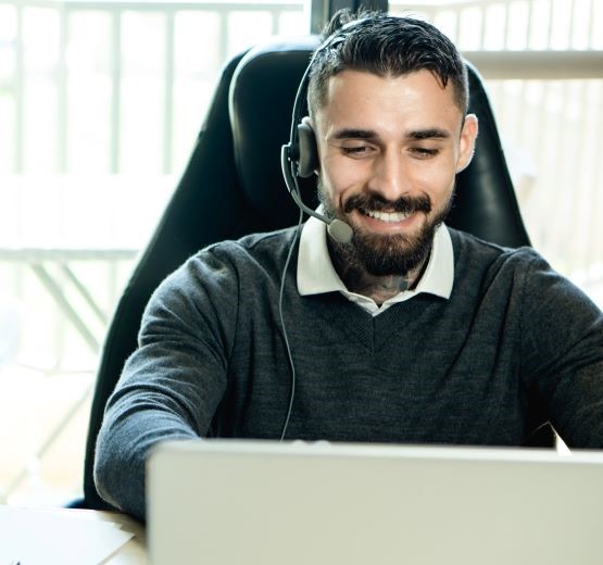 Man in customer service department wearing a headset and smiling while speaking to a customer, because he can see the full history in Dynamics 365.